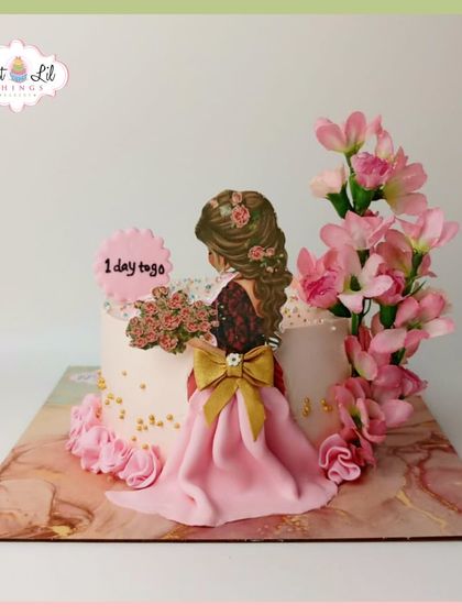 A beautiful cake for a bride-to-be, featuring a fondant dress, fresh pink flowers, and a "1 day to go" sign.