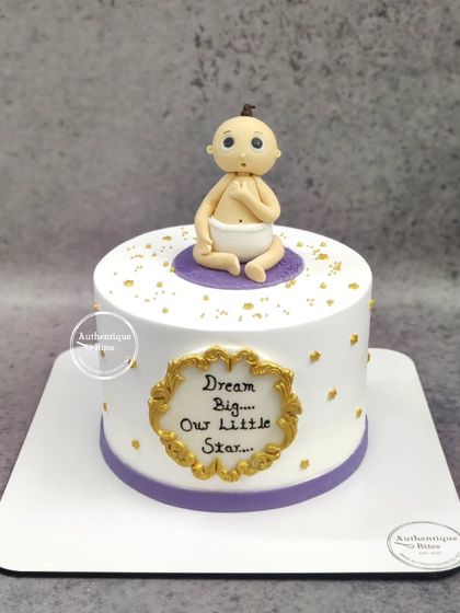 A simple and sweet cake to welcome a new baby. The cake features a small baby figurine and a plaque that reads "Dream Big... Our Little Star."