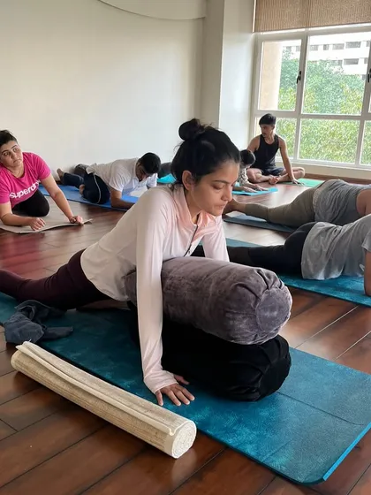 Students using bolsters to support them in a forward fold variation. This demonstrates how props can be used in a group setting to help everyone find a safer and deeper stretch.