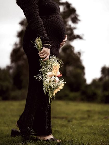 A close-up detail shot of the mom-to-be holding a bouquet of flowers, with the focus on her baby bump and the delicate blooms.
