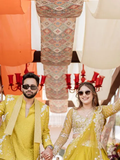 The couple making a grand entrance at their carnival, hand in hand. They are both dressed in vibrant yellow, looking bright and happy.