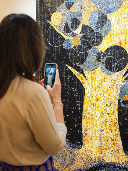 A visitor takes a photo of a vibrant, textured painting by Eva Malhotra, capturing the intricate details of her work.