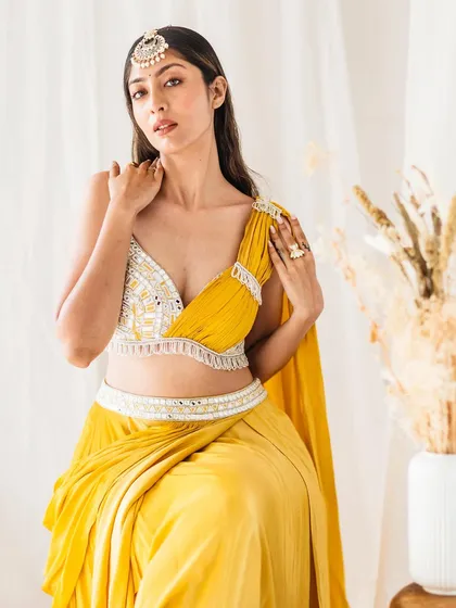 A seated portrait from a fashion shoot, this image showcases a draped yellow outfit. The composition is focused on the elegant fall of the fabric and the detailed craftsmanship of the belted waist and blouse.