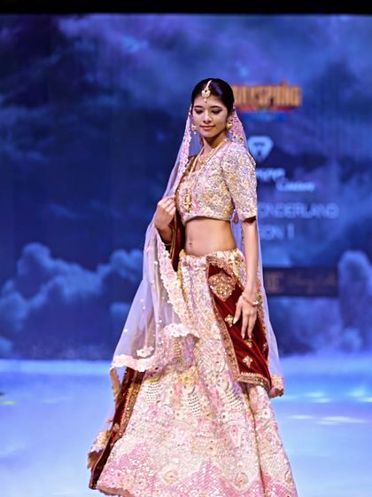 A soft pink lehenga with heavy silver and gold embroidery, paired with a rich maroon velvet accent. This design balances delicate color with opulent craftsmanship.