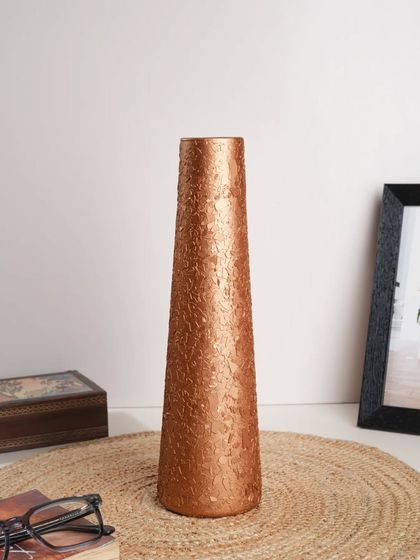 A tall, slender copper vase styled in a minimalist home office setting. This shows the product's versatility in different environments.