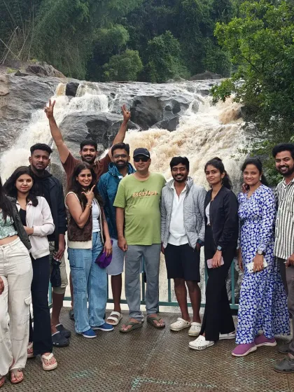 A group posing on a bridge in front of a beautiful waterfall in Munnar. Our trips to Kerala also feature some stunning cascades.