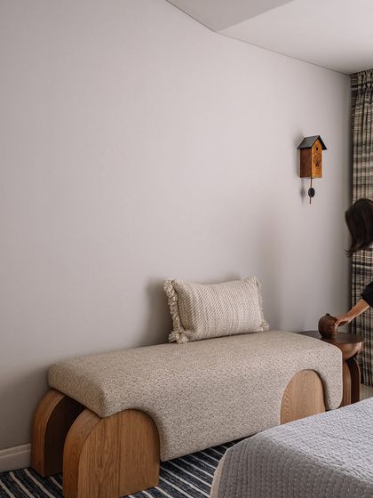 A detail of the guest bedroom, showing a custom upholstered bench and a cuckoo clock, adding a touch of whimsy to the serene space.