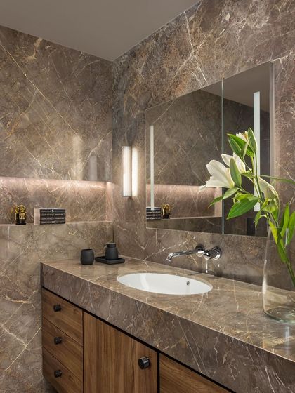 A wider view of the brown marble bathroom in the West Coast Residence, showcasing the full-height stone slabs and the custom wooden vanity.