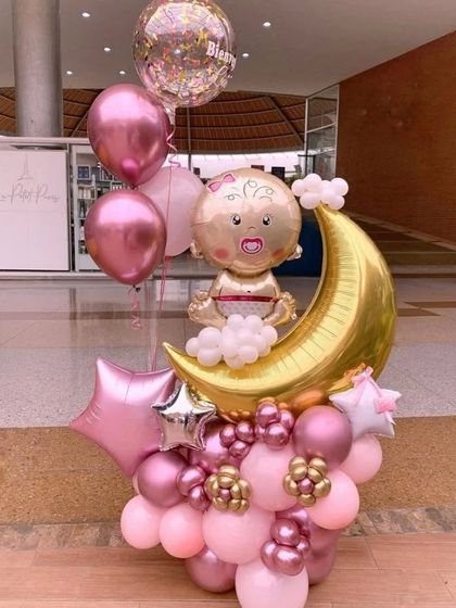 An adorable baby shower balloon bouquet in pink, featuring a baby on a moon foil balloon as the centerpiece.