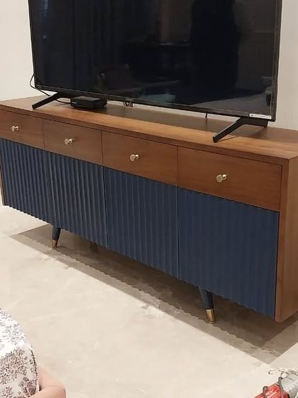 A direct view of the two-tone TV unit, showcasing the contrast between the smooth wood drawers and the textured blue cabinets. The small brass knobs are a perfect finishing detail.