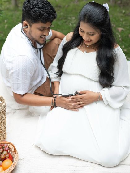 A playful and sweet moment during a picnic maternity shoot. The dad to be listens to the baby's heartbeat with a stethoscope, adding a personal and charming touch.