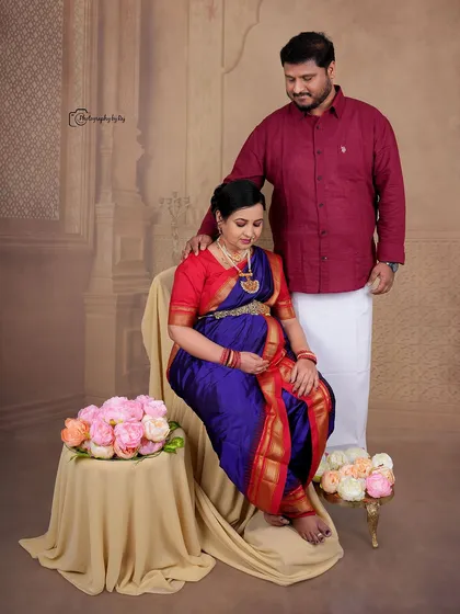 A regal studio portrait of a couple in traditional Maharashtrian attire, seated gracefully with floral props.
