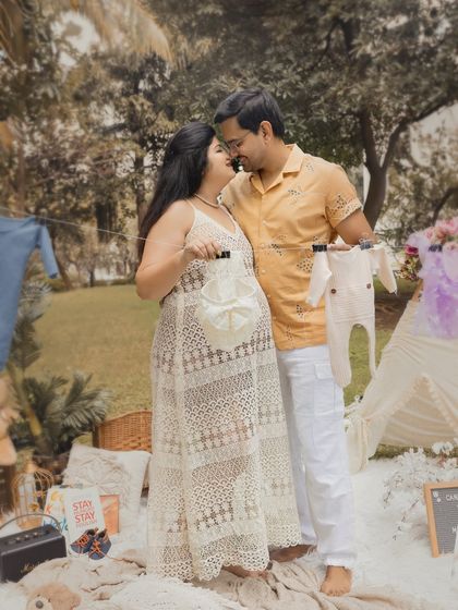 A playful and cute photo idea for an outdoor shoot. The couple holds up a line of baby clothes, dreaming of their little one's arrival.