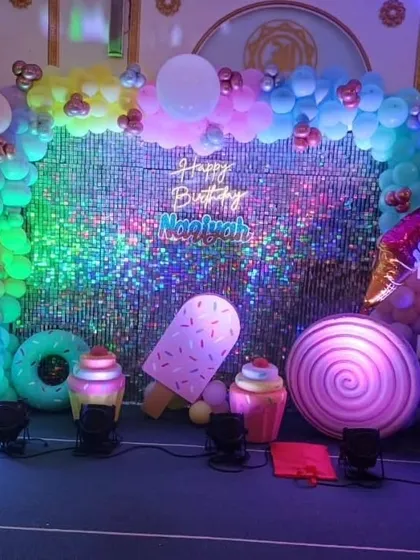A Candyland theme featuring a shimmering sequin backdrop, a neon birthday sign, and large illuminated props like an ice cream bar and a lollipop.