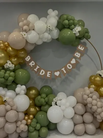 A lovely rustic-themed bridal shower decoration. The olive green, beige, and gold balloons are complemented by a simple 'BRIDE TO BE' banner.