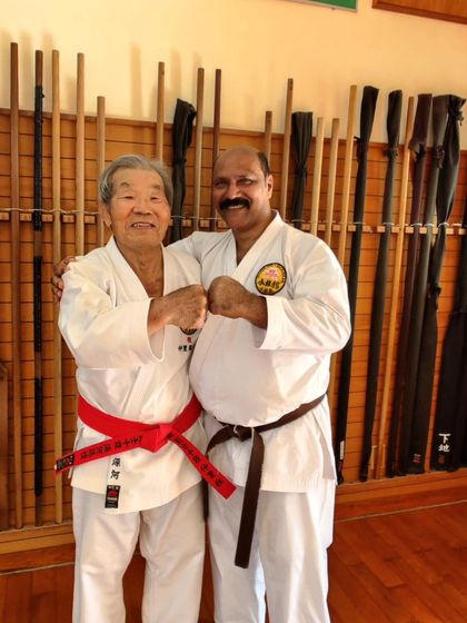 A moment of camaraderie with a senior master at the Honbu Dojo, in front of the dojo's weapon rack.