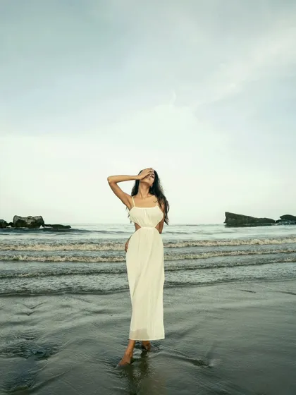 A wide shot that captures the expansive feel of the beach and sky. The model stands as a solitary, elegant figure against the vastness of the landscape.