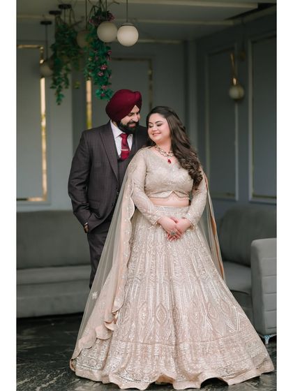 A full-length portrait showcasing the couple's coordinated outfits and the bride's stunning lehenga. Their shared look of affection completes this beautiful engagement photo.