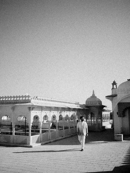 A solitary, thoughtful moment for the groom, captured in timeless black and white. This wide shot shows him walking alone in the palace courtyard, creating a sense of peace and anticipation.