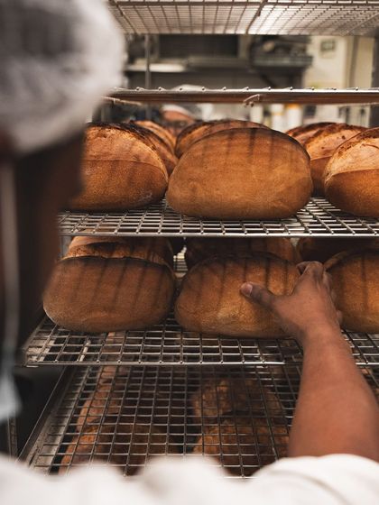 A baker checks on racks of freshly baked sourdough loaves, a key part of our deli and sandwich offerings.