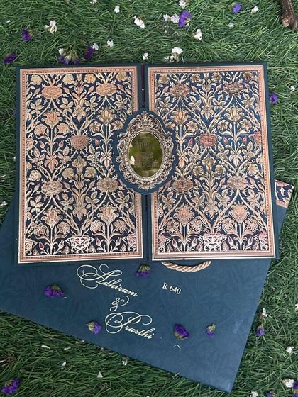 This gate-fold card features a stunningly intricate brocade pattern in deep blue and gold, with a central emblem holding the invitation closed.
