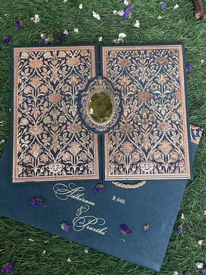 This gate-fold card features a stunningly intricate brocade pattern in deep blue and gold, with a central emblem holding the invitation closed.