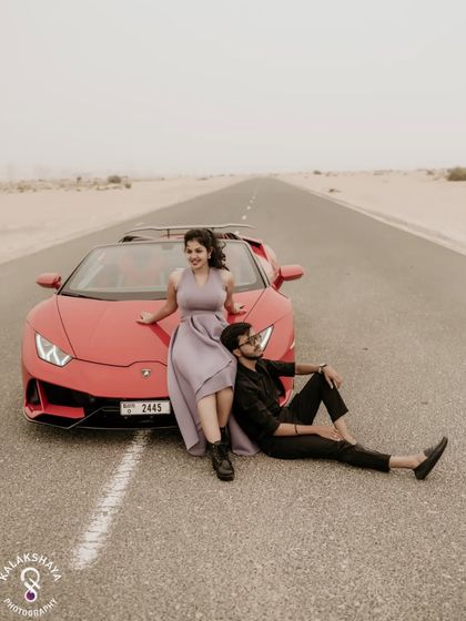 A full-length shot of the couple with the red Lamborghini, showcasing their style and the stunning location.