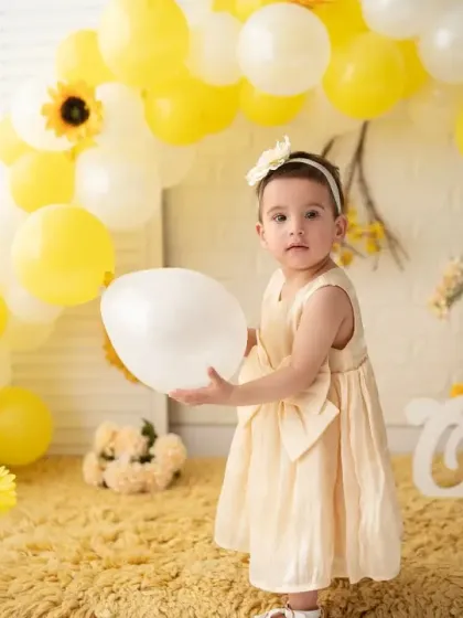 A full-length shot of the birthday girl in her pretty yellow dress, standing amidst a balloon arch. Our sets are designed to create a complete, festive scene.
