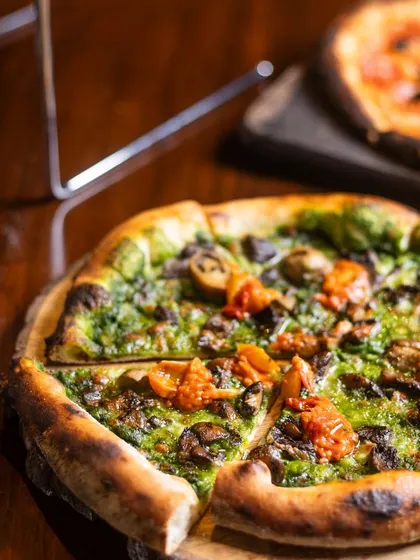 A slice of our Mushroom pizza with a vibrant green sauce, ready to be enjoyed. The combination of flavors is truly unique.