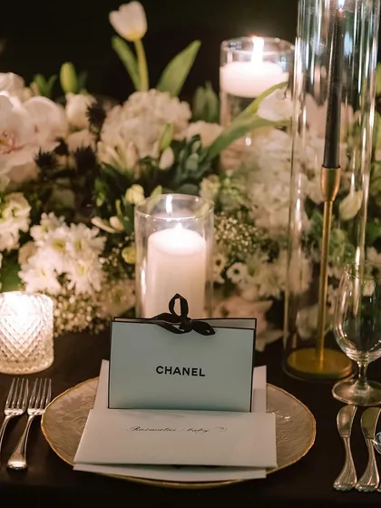 A close-up of the Chanel-themed place setting, with a personalized menu and a chic favor box, surrounded by white flowers and candles.