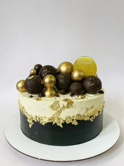 This black, white, and gold cake is all about modern elegance. The design uses a fault line style, edible gold leaf, and a cluster of chocolate and gold spheres for a bold, graphic look.