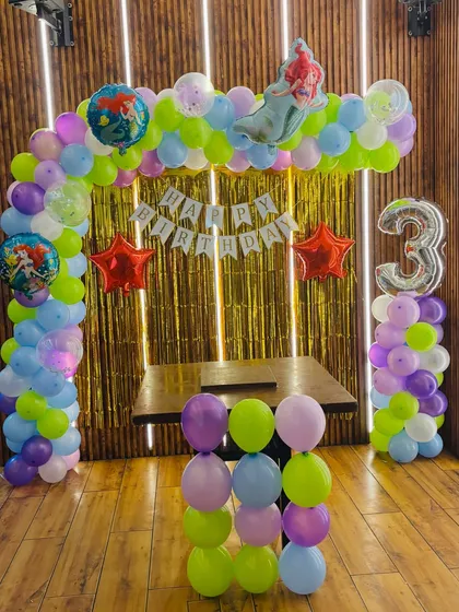 A magical mermaid-themed birthday party for a 3-year-old. The balloon arch uses pastel colors, and features Ariel and other sea-themed foil balloons.