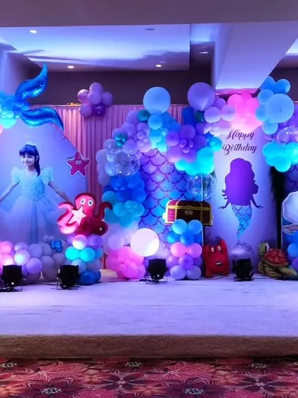 A spectacular mermaid themed stage with characters from "The Little Mermaid." The decor uses shades of purple, blue, and pink balloons to create a magical underwater effect.