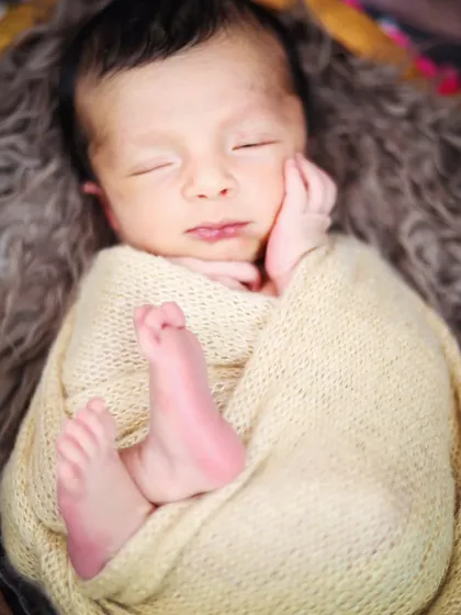 An intimate close-up of a newborn's face and feet, wrapped snugly in a soft blanket. These are the moments you'll want to hold onto.
