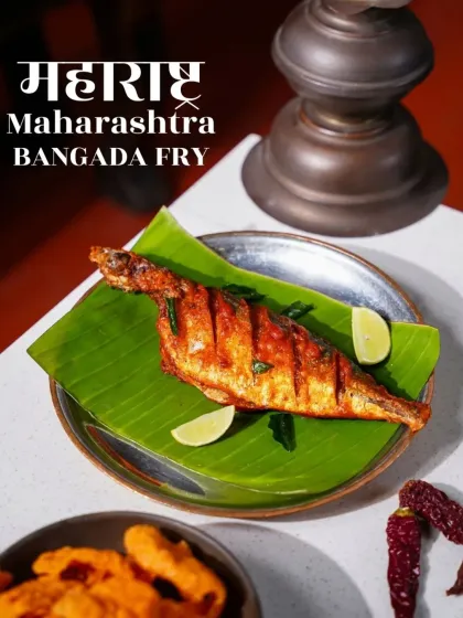 A perfectly fried Bangda (mackerel) served on a banana leaf, representing Maharashtrian coastal cuisine. The graphic text overlay makes this a great image for a menu or promotional campaign.