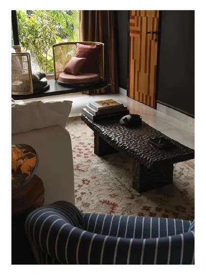 A view into the lounge space of our home, where a rotatable swing and a carved dark wood coffee table create a relaxed yet sophisticated corner. The patterned door, crafted with inlaid wood, adds another layer of texture and craftsmanship, showcasing our belief in custom, handmade elements.