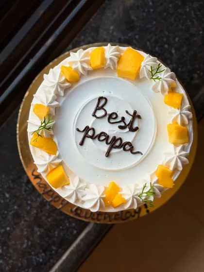 A closer look at the "Best Papa" mango cake, showing the fresh mango pieces and delicate green sprigs.