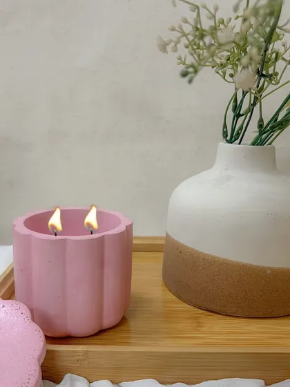Our pink Daisy Jar, double-wicked for an even burn, creating a cozy ambiance next to a vase of flowers.