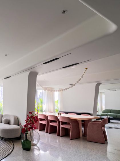The open-plan dining area in Apartment 56 takes center stage. The volumetric, powder-pink velvet chairs and matching table add warmth and texture to the cool, minimal canvas of white walls and terrazzo floors.