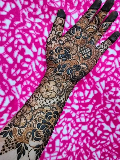 A full-sleeve floral design against a vibrant pink background. The contrast makes the intricate details of the henna pop.