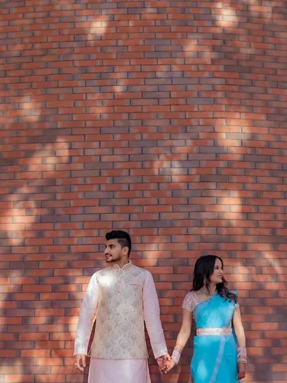 A stylish, composed shot of a couple holding hands against a modern brick wall, with beautiful light and shadow play.