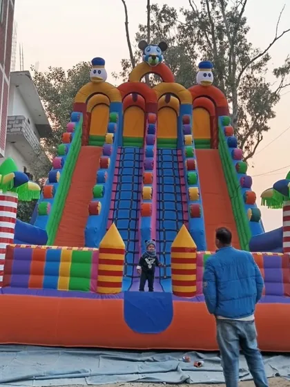 Here is our 4-lane colorful bouncy slide set up outdoors. You can see how tall and impressive it is, with people standing next to it for scale.