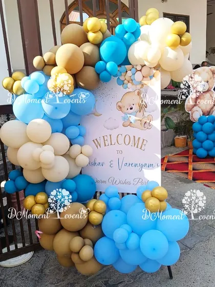A welcome sign for a twins' baby welcome party with a teddy bear theme. The sign is framed by a beautiful arrangement of blue, beige, and white balloons.