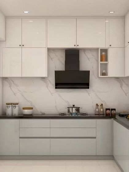 A U-shaped modular kitchen with all-white, high-gloss cabinets and a black countertop. The white marble-effect backsplash adds a touch of luxury, while the layout provides an efficient and organized workspace.