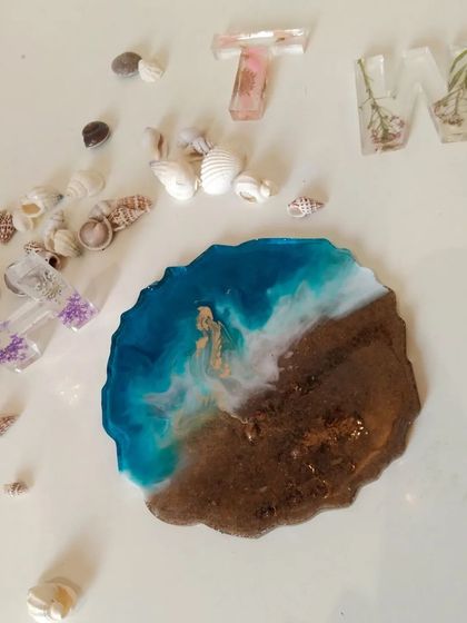 An overhead shot of the beach scene coaster, surrounded by seashells and custom resin initials, showing how different pieces can create a cohesive theme.
