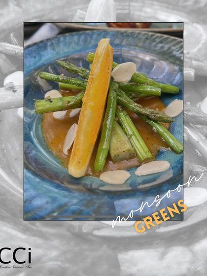 A celebration of fresh, seasonal ingredients. This 'Monsoon Greens' dish features tender asparagus spears and a slice of citrus arranged on a flavorful sauce, topped with almond slivers for a delightful texture.