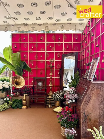 A vibrant photo corner with a fuchsia pink backdrop featuring gold block prints and hanging bells. The space is furnished with antique wooden pieces and a vintage gramophone.