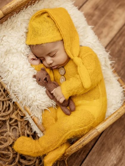 An overhead shot showing the baby boy snuggled up in his cozy yellow outfit, holding his teddy bear close.