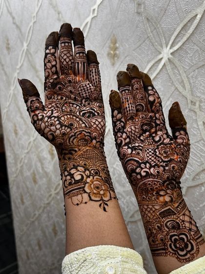 An intricate and dense bridal henna application for a fellow makeup artist. The design is packed with florals, paisleys, and fine-line details, covering the hands and extending up the arms.