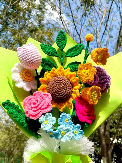 A beautiful outdoor shot of the vibrant mixed flower bouquet. The natural light makes the colors of the crochet sunflower, roses, and tulips look even more lively.